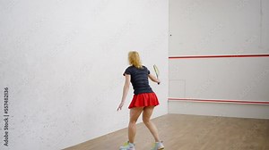 Fit woman in tennis skirt plays squash on four-walled court