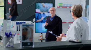 Elderly shopper watching pharmaceutical product advertising on digital screen in apothecary, approaching pharmacist with intention of buying advertised drugs. Expert assists senior customer with info
