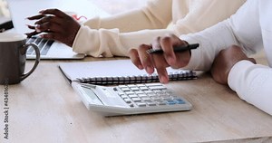 Woman working on laptop with husband using calculator and writing in book on desk at home