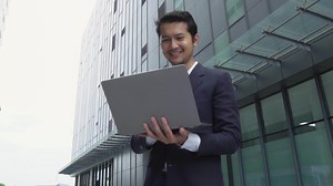Download Asian businessman using laptop working on investment, high rise building background, for free