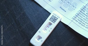 Covid 19 positive at home test kit on black table with instruction book pamphlet showing how to find positive results with two red lines close shot panning around and up with transition out.