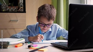 distance learning. a teenage student is studying on a laptop. writing down a synopsis in a notebook. sitting at home at the writing desk