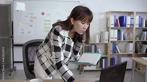 woman ceo standing in the office is bending over and looking up information on the computer after reading a memo in the notepad with concentration.