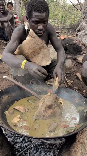 Cooking meat over open fire, Hadzabe men celebrate the success of their hunt.