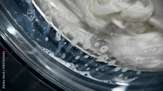 An automatic washing machine washes dirty white clothes. Washing clothes in a domestic washing machine. Close-up video of the spinning drum of a washing machine.