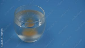 Vitamin C effervescent tablet dissolving in glass of water on blue background. Copy space for text.