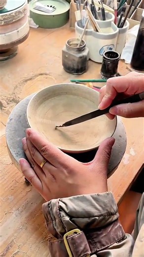 Metal tool etches clay bowl—rotating wheel guides steady sculptor’s hand