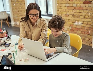 Learning to code. Smiling young female teacher in glasses showing scientific robotics video to little boy, using laptop in classroom Stock Photo - Alamy