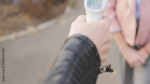 Close-up of a schoolgirl's temperature measurement using an electronic thermometer in front of school during the pandemic.