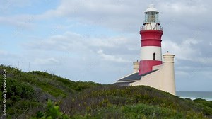The red and white striped light tower of the historic Cape Agulhas lighthouse at the southern tip of Africa where the Indian and Atlantic oceans meet during a cloudy day.