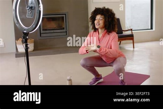 While adjusting ring light mount, African American woman filming squats on mat at home for fitness. Fitness, home workout, training, active lifestyle, wellness, exercise, self-care Stock Video Footage - Alamy