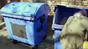 Homeless man with shopping cart digging in trash can.