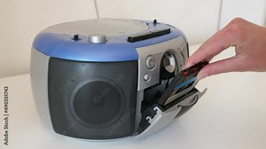 female inserting audio cassette in portable radio and pushes play, static side view, closeup