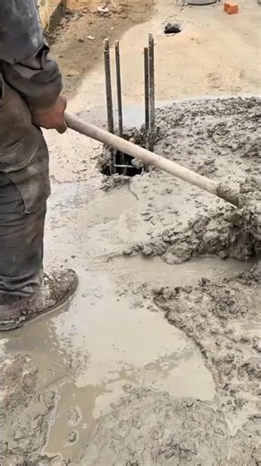 leveling wet concrete on the ground using a long wooden tool to create a smooth and even surface