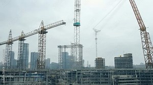 Construction progress on a high-rise building with cranes operating in an urban setting during overcast weather