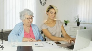 young woman helping an old senior woman doing paperwork and administrative procedures with laptop computer at home