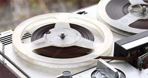 Analog reel-to-reel tape recorder plays a melody by rotating reel-to-reel cassettes on a vintage music player from the 70s, close-up