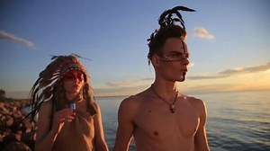Beautiful native american Indian man and woman in traditional dress walking sea beach at sunset.