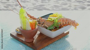 Gourmet seafood platter with fresh lobster, shrimp, and salmon served on wooden board, complemented by variety of vegetables and sauces, showcasing luxury dining by seaside. Fine dining experience.