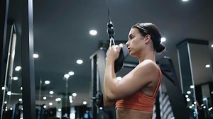 Side view of fitness woman working out in gym doing exercise for biceps. Athletic girl training. Woman on rowing machine for health, wellness, body. Multi station at gym for arm, shoulders muscles.