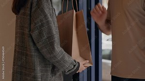 Unrecognizable delivery man hands a paper food bag to a female client at her home, showcasing a safe delivery service.