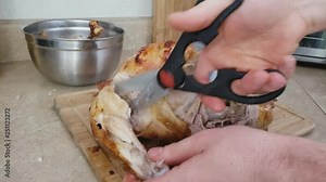 Home cooking - Cutting into freshly roasted Turkey using kitchen shears and transferring portion to bowl. Just removed from electric counter top rotisserie and skewer and placed on wooden board.