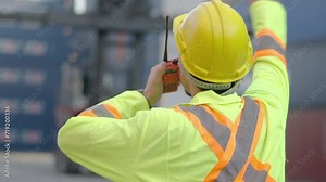 Asian foreman in hardhat and safety vest talking on the walkie-talkie control loading Containers box at warehouse logistic in Cargo freight ship for import export in harbor, shipping loading in docks