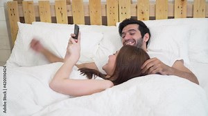 Footage b roll of Couple using smart phone and happy on bed. Beautiful couple sitting on the bed and looking photo from the trip on smartphone, touching screen, Watching movie or chatting app.