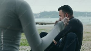 Athletic young man performs a Russian abs twist with a fitness ball, supported by a female friend outdoors, illustrating the power of teamwork in fitness