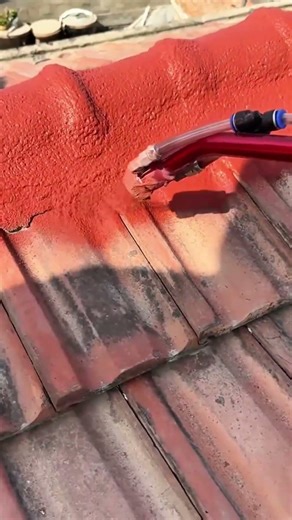 Applying a fresh coat of red protective sealant to weathered clay roof tiles using a high pressure