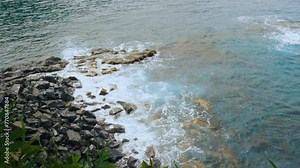 Waves slowly roll over black rocks of a volcanic beach. A view of tidal wave near the shore. Rocky beach and waves of Honolulu Nui Bay in Maui island, Hawaii.