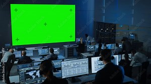 Big Green Screen Horizontal Mock Up in a Control Center Room with Engineers and Controllers Working on Computers. Team of Telecommunication Employees Work in Monitoring Room Full of Displays.