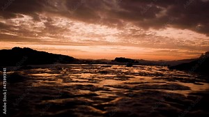 Rock pool water runs back to the ocean, golden sky with a fire sunset