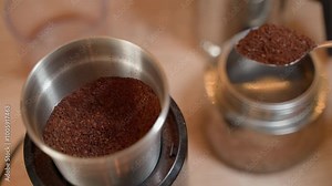 Freshly ground coffee is taken with a teaspoon from a coffee grinder and poured into a geyser coffee maker, close-up