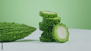 Slow motion shot of a fresh green bitter melon and a stack of round slices of bitter melon. Bitter melon (Momordica charantia) tea could support in the treatment of diabetes