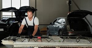 Male Technician Inspecting And Repairing An Electric Vehicle Battery In A Modern Auto Repair Shop Environment. Auto Service, Electric Car Battery Handling. EV Car Battery In Workshop