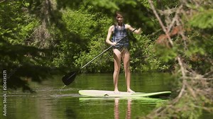 stand up paddle girl focus through trees on river 4k