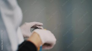 Scientist in white robe and rubber gloves using air compressor on wet glass lens at laboratory, close up