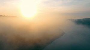 Fantastic scenery of misty river in sunny beams. Aerial view from drone of mystery valley with meandering foggy river flowing between hills with scenic sunset on background. Concept of landscape