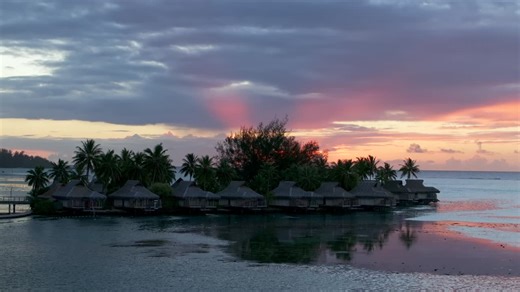 Stunning vibrant pink orange sunset sun rays Sofitel Kia Ora Resort Bungalow villas Moorea island French Polynesia aerial drone Cooks Opunohu Bay lagoon coral reef Pacific Ocean circle right parallax | Premium Stock Video Footage