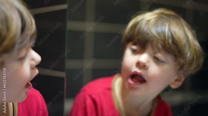 Child stares at bathroom mirror checking mouth and teeth, little boy opening mouth looking at his reflection