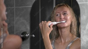 Portrait of young woman brushing her white teeth with modern electric toothbrush, close-up. Concept of dentistry, daily care, oral hygiene and teeth cleaning. morning procedures in healthcare,
