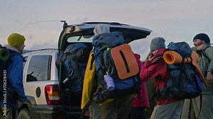 Diverse hiking buddies arrive to rental house on car. Happy tourist friends talk and take backpacks from trunk. Group of tourist during trip or expedition to mountains on vacation. Outdoor activities.