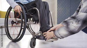 Girlfriend helping her paraplegic boyfriend. Care and disability concept. Woman helps paralyzed legs of a disabled person sitting in a wheelchair.