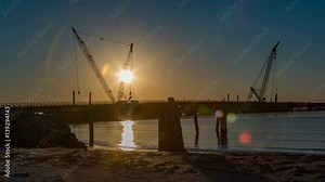 Construction Sunset on Herbert C Bonner Bridge in Outer Banks NC with Cranes and Sunlight Reflection on Ocean Inlet Water while Vehicles are Driving Over