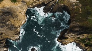 Static aerial view of Pacific Ocean waves crashing against rocky cove, Oregon coast.