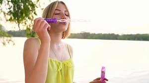 Young beautiful blonde blowing soap bubbles outdoors