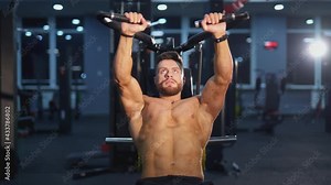Training muscles. Sportsman pumping his trained body on a simulator. Strong trainer doing workout. Bodybuilder doing exercise on the modern simulator in the gym.