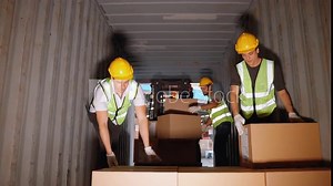 Workers load boxes of goods into containers at a distribution center.