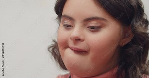 Portrait of adorable teen girl having down syndrome. Close up view of brunnette pretty girl with wavy hair with genetic disorder. Concept of people, emotions and sunny children.